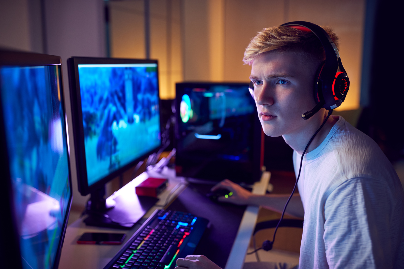 Teenage Boy Wearing Headset Gaming at Home Using Dual Computer S